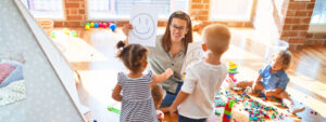 psychologist and group of toddlers make therapy using emotions emojis around lots of toys at kindergarten
