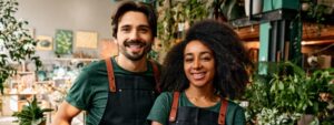 Family business of gardeners. A man and a woman in professional clothes are standing in their own plant shop and smiling.